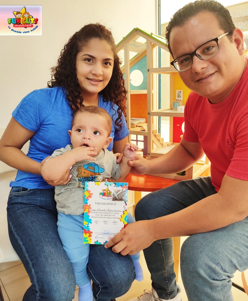 Papa y mama sosteniendo a su hijo con su certificado de primer corte de cabello en Fun Cuts Nicaragua